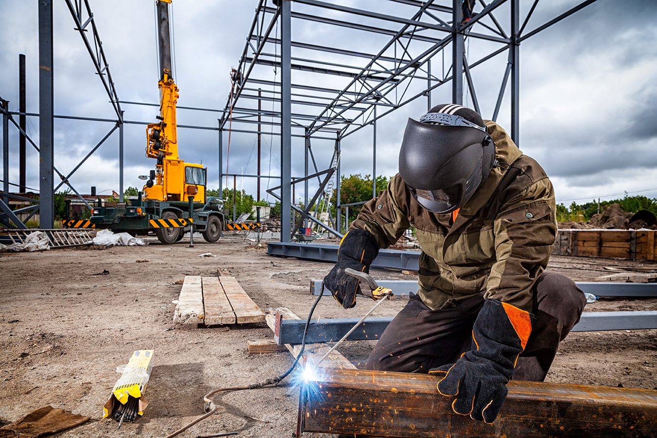 A young  man welder in brown uniform, welding mask and welders l