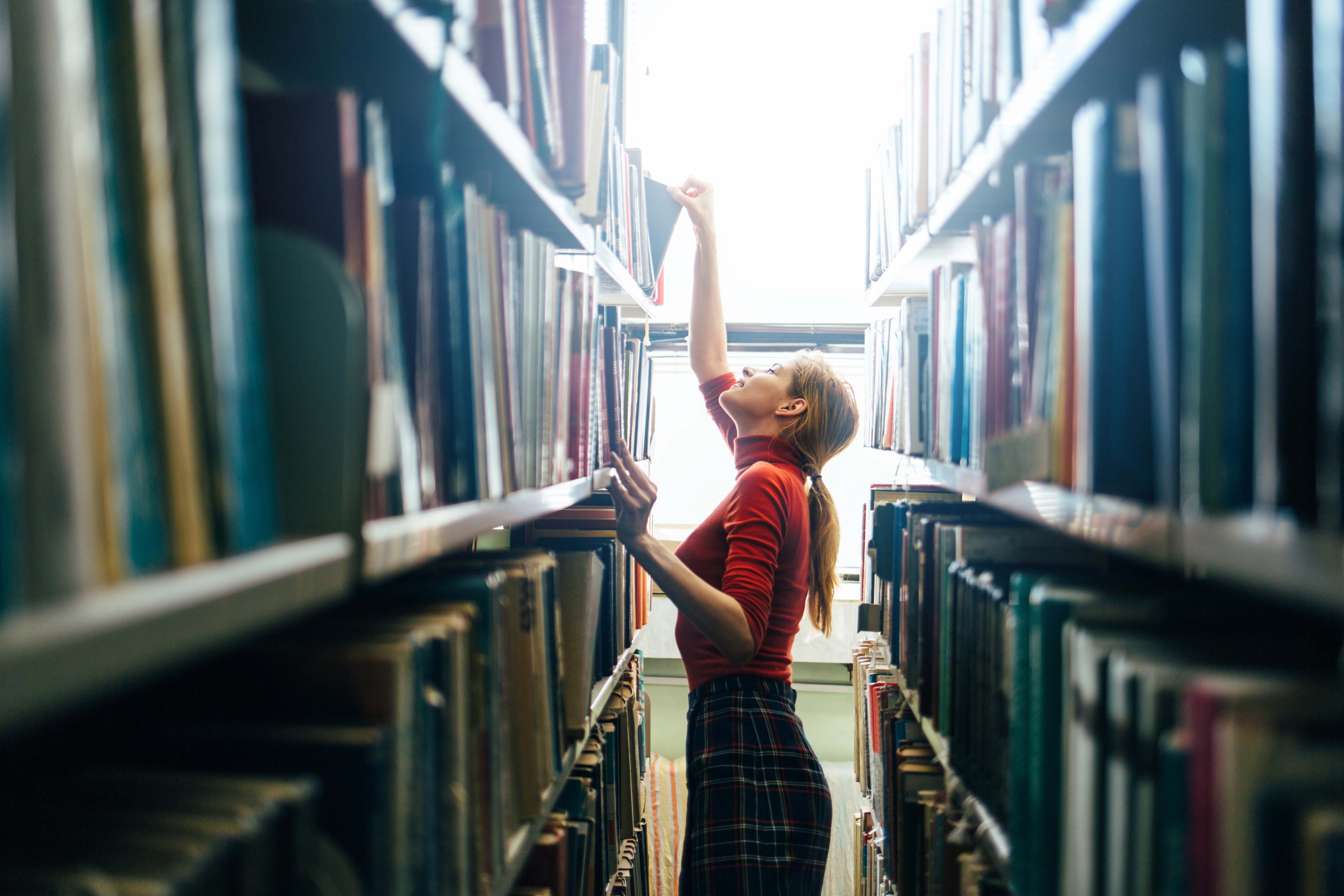 Young librarian searching books and taking one book from library