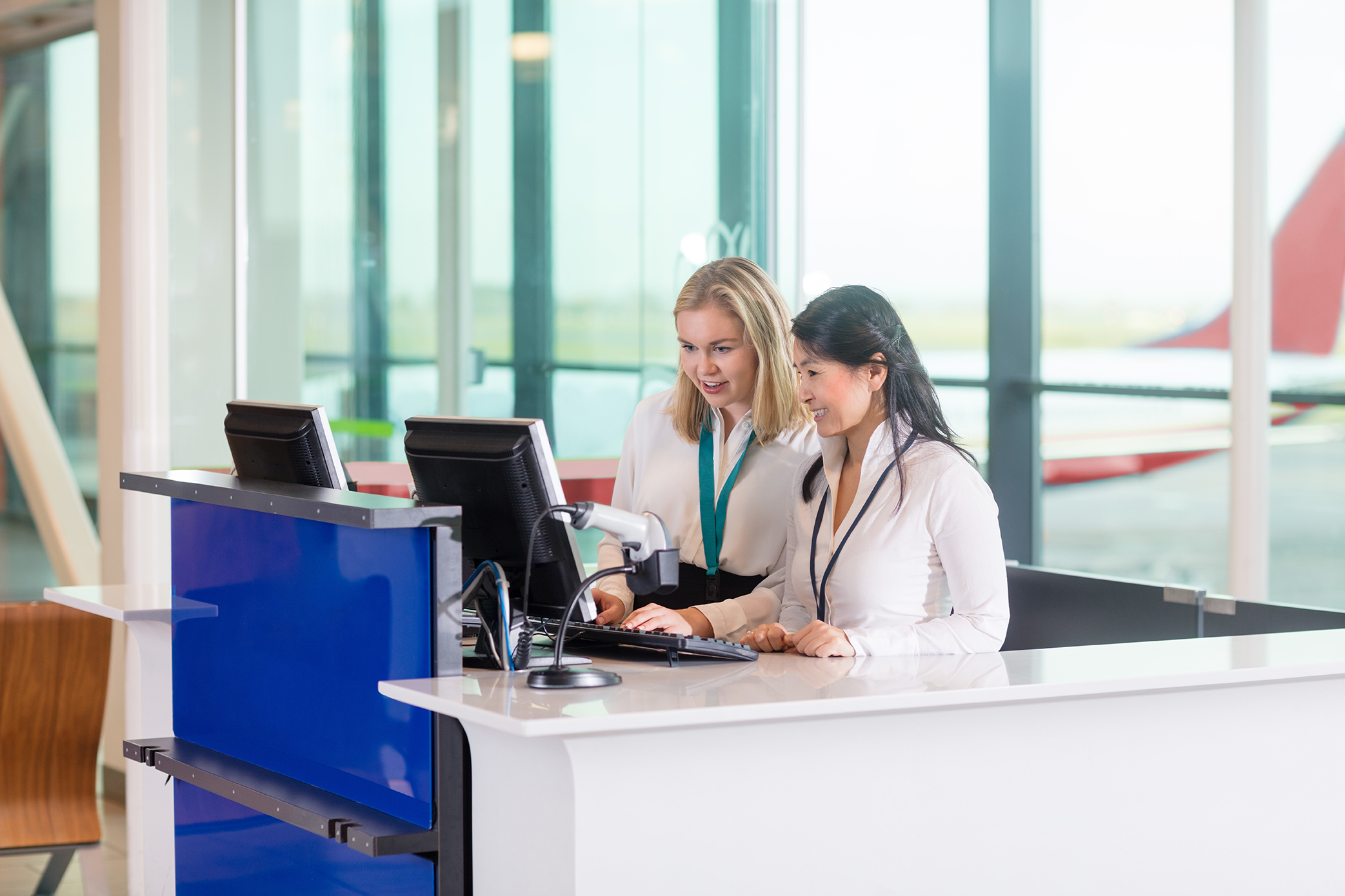 Receptionists Using Computer At Counter In Airport