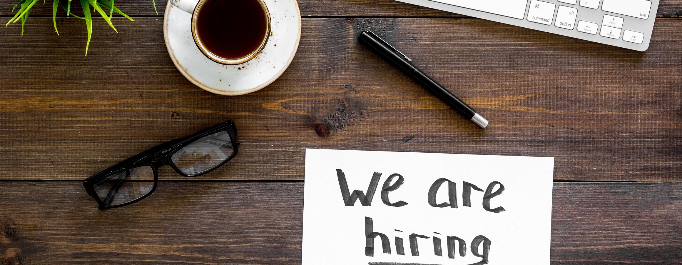 Search for worker, employee concept. We are hiring lettering on work desk on dark wooden background top view copy space