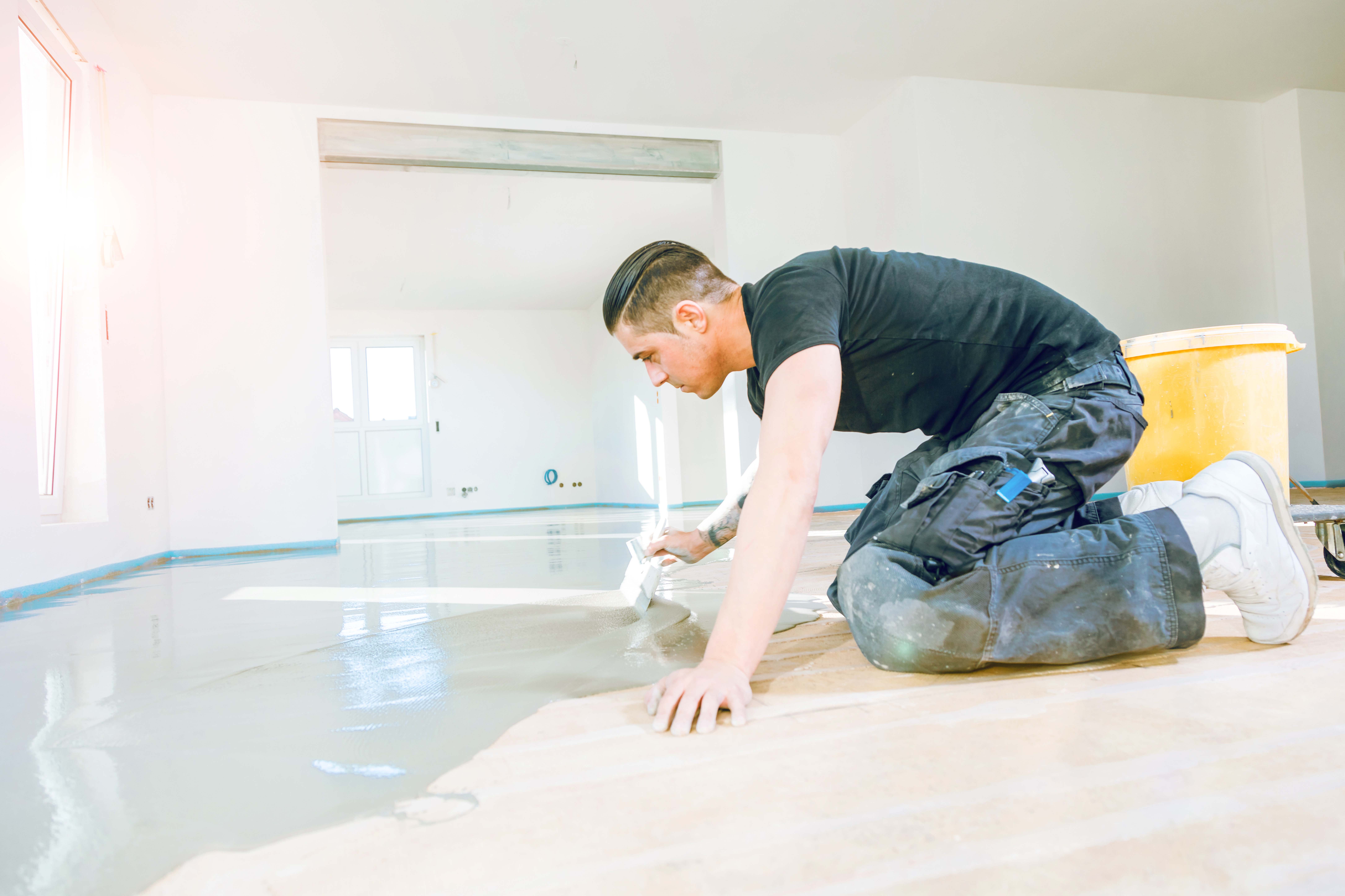 Plasterer during floor covering works with self-levelling cement mortar