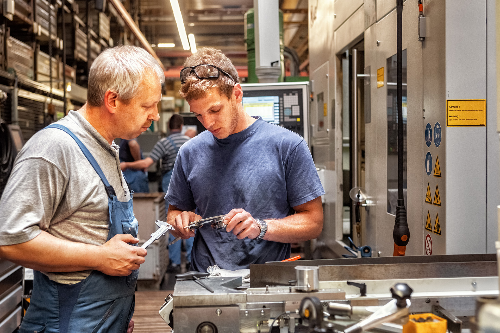 Skilled workers standing in a production hall in front of a mach